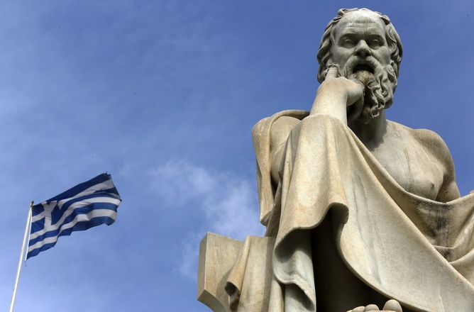 A Greek flag flutters by a statue of ancient Greek philosopher Socrates in Athens