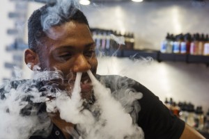 A sales clerk exhales vapor while smoking with a vaporizer during a wait for customers at the e-cigarette shop Henley Vaporium in New York, June 23, 2015. REUTERS/Lucas Jackson  - RTX1HS5K