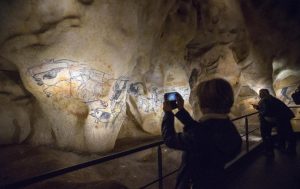 A visitor takes pictures of a replica of pre-historic animals drawings seen on a wall during a press visit of the Cavern of Pont-d'Arc project site in Vallon Pont d'Arc