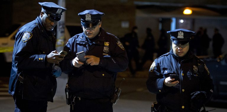 Police look at social media apps on their smart phones at the scene of a shooting where two New York Police officers were shot dead in Brooklyn, New York