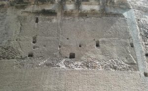 In this photo you can see the outer brick layer (bottom), the exposed inner concrete (middle to top), and the holes used to support scaffolding and framework during construction.