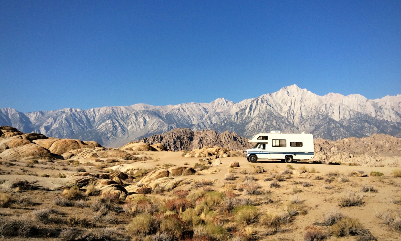 Travel Trailer On Field By Rocky Mountains Against Clear Blue Sky