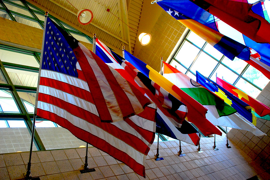  A row of flags of different countries hangs from the ceiling of a building.
