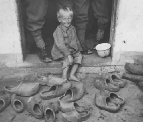 This little Dutch boy is pictured with the family wooden shoes with soldiers standing behind him