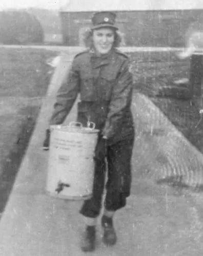 Liz posed with a coffee urn and a smile in the very cold winter of December 1944, at Camp Dane Ghyell in northern England