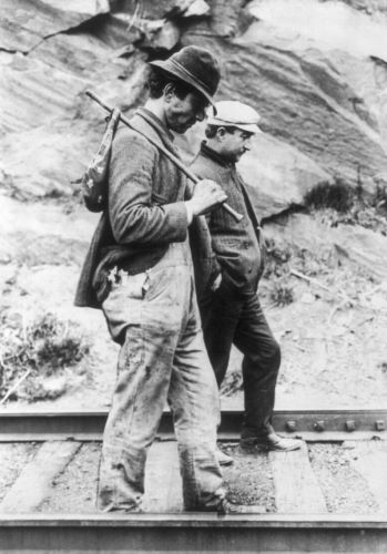 Two hoboes, one carrying a bindle, walking along railroad tracks after being put off a train (c. 1880s–1930s)