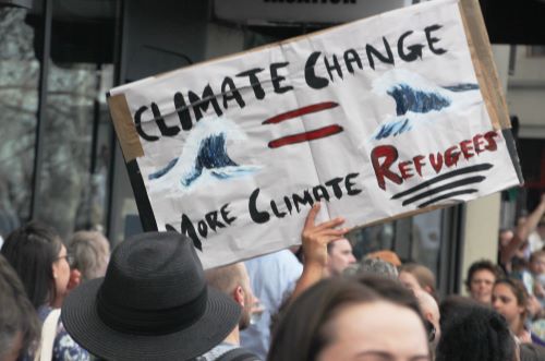 An activist holding a sign "Climate change = more climate refugees"