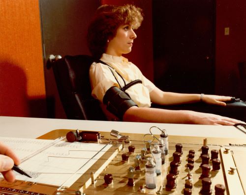 Demonstrating the administration of the polygraph, the polygrapher making notes on the readouts. 1970s.