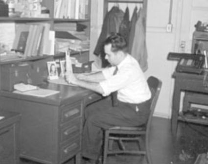 Engineer using a slide rule, with mechanical calculator in background, mid 20th century