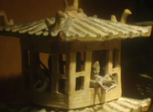 A miniature guard brandishing a handheld crossbow from the top balcony of a model watchtower, made of glazed earthenware during the Eastern Han